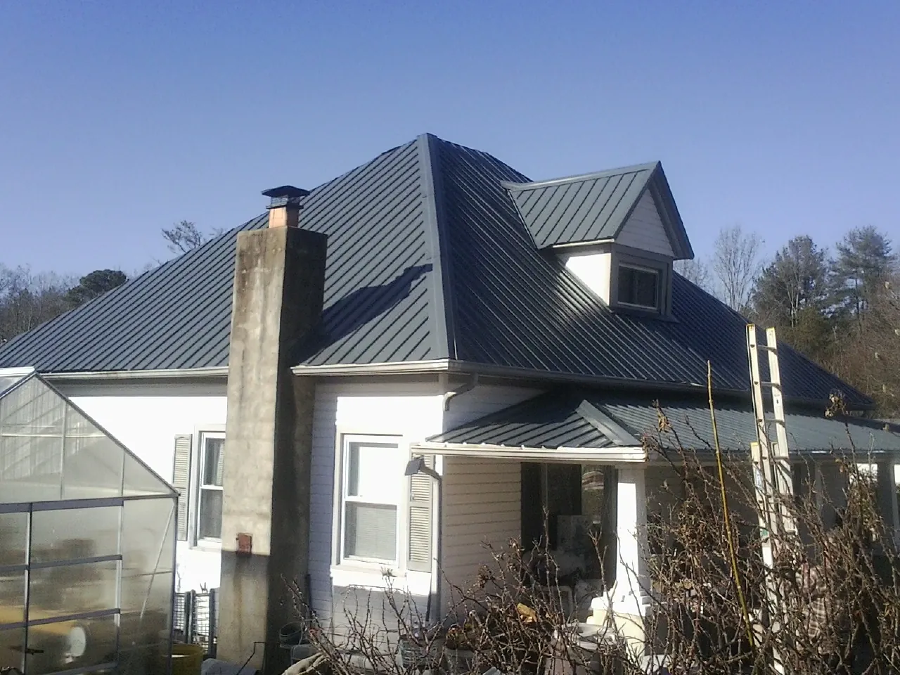 Dark blue standing seam metal roof on a white farmhouse with dormer — Slate & Tile Roof Repair by Roofing Brothers in Viborg