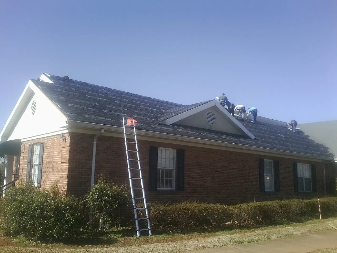 Crew tearing shingles off a brick ranch roof with a ladder set — Metal Roof Repair work by our crew in Viborg
