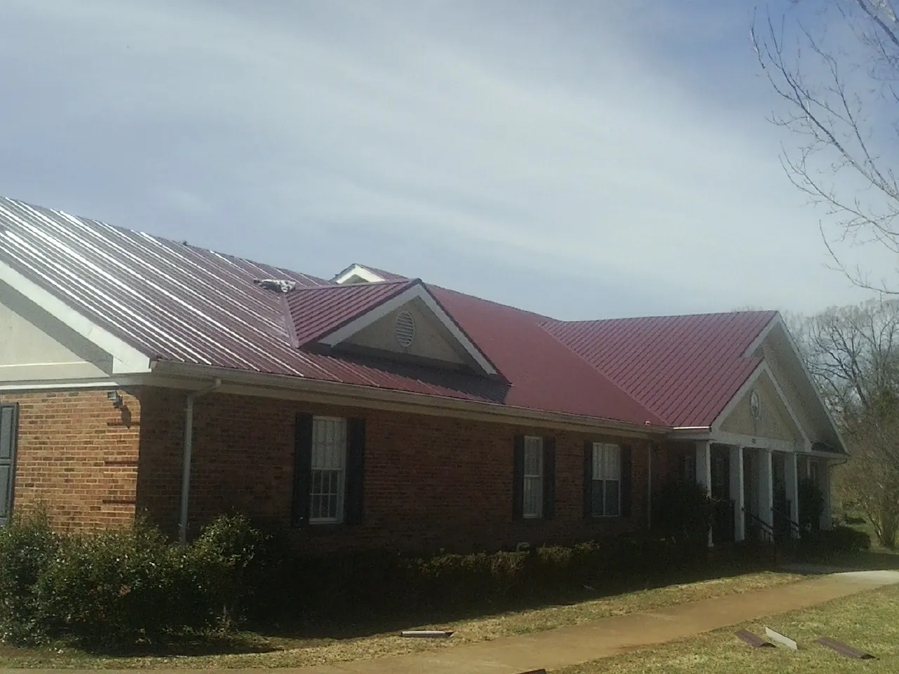 Red metal roof with gabled entries on a long brick building, from a Hail Damage Roof Repair job in Viborg