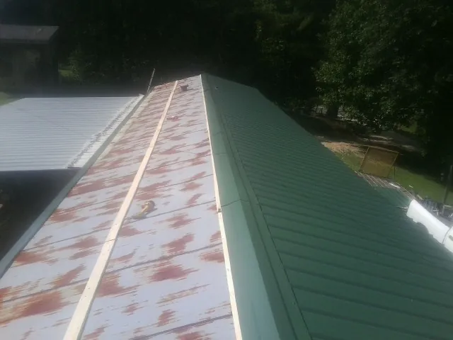 Old rusted panels beside newly installed green metal roofing — Wind Damage Roof Repair by Roofing Brothers in Viborg