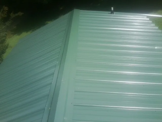 New green metal panels meeting at the ridge of a roof — Flat Roof Repair work by our crew in Viborg