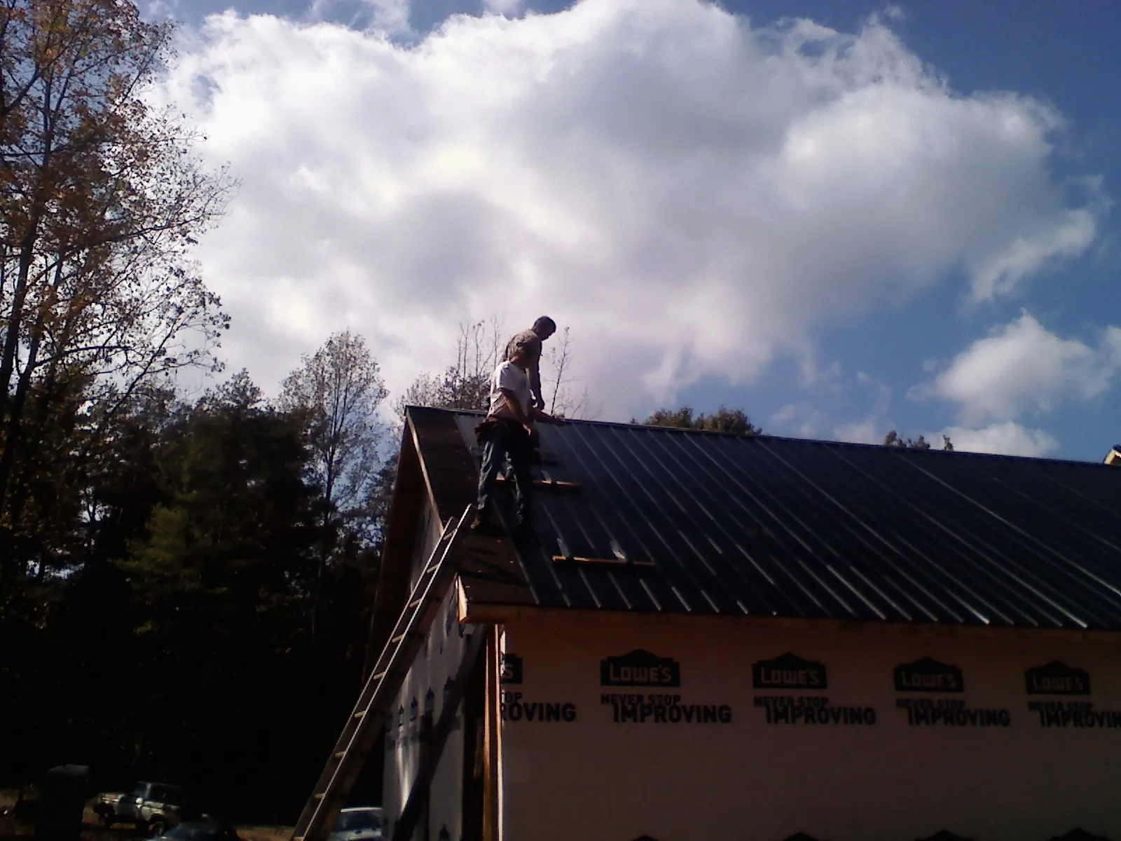Roofer fastening dark metal panels high against a cloudy sky, from a Roof Inspection job in Viborg