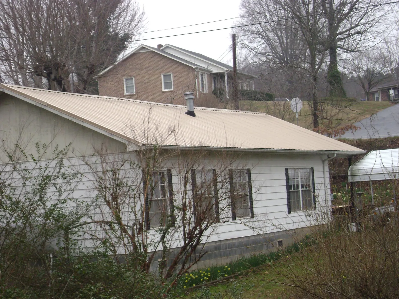 Tan metal roof on a white sided house set into a hillside — Commercial Roofing by Roofing Brothers in Viborg