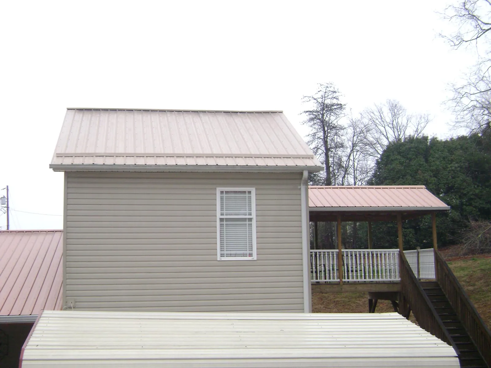 Tan metal roofs on a two story addition and attached porch, from a Roof Replacement job in Viborg